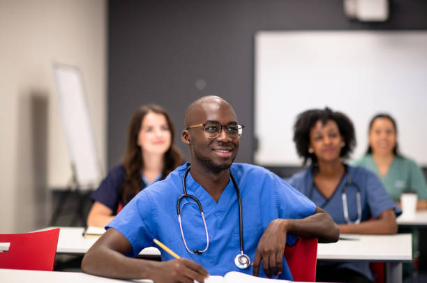 A diverse group of students dressed in medical wear learn in a classroom setting.